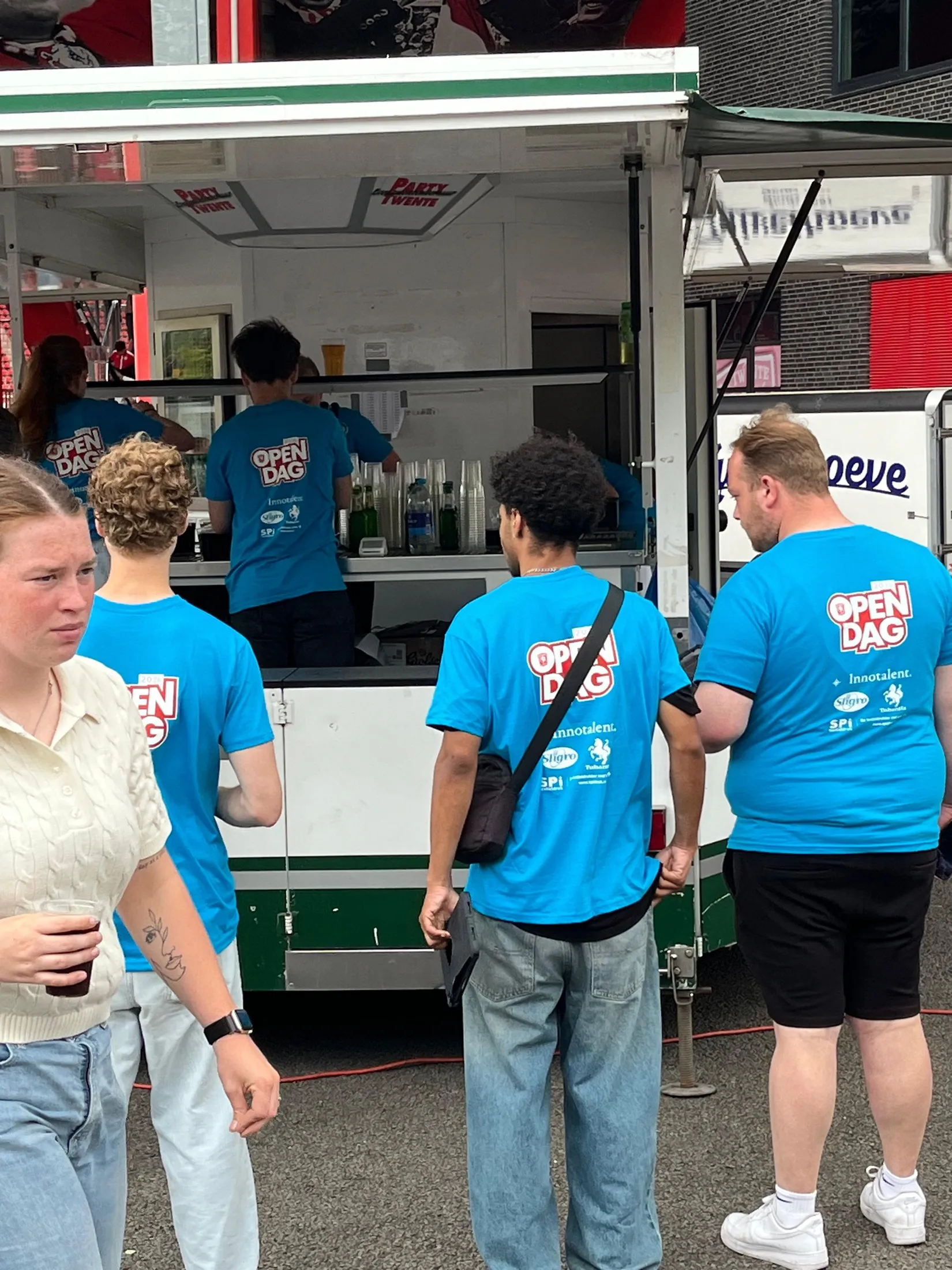Crew members in blue Open Day shirts carrying the name Innotalent, at a bar during the FC Twente Open Day.