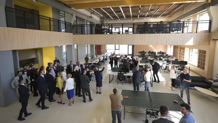 Inside Tech Park Prishtina: an open, double-height workspace with desks on a wood-lined mezzanine, a ping-pong table, and people gathered below.