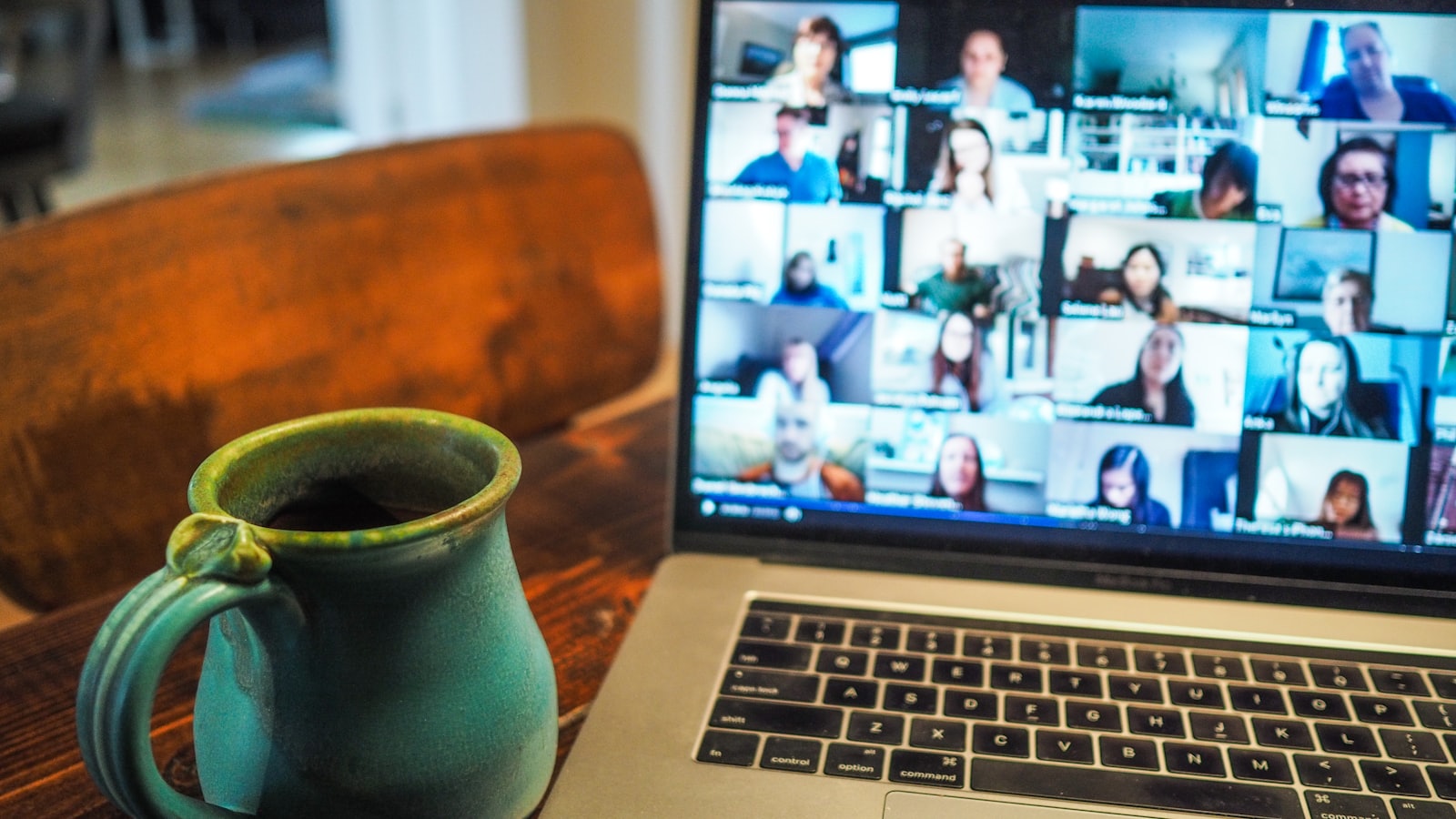 Een laptop met een videogesprek in rasterweergave naast een mok koffie op een houten bureau.