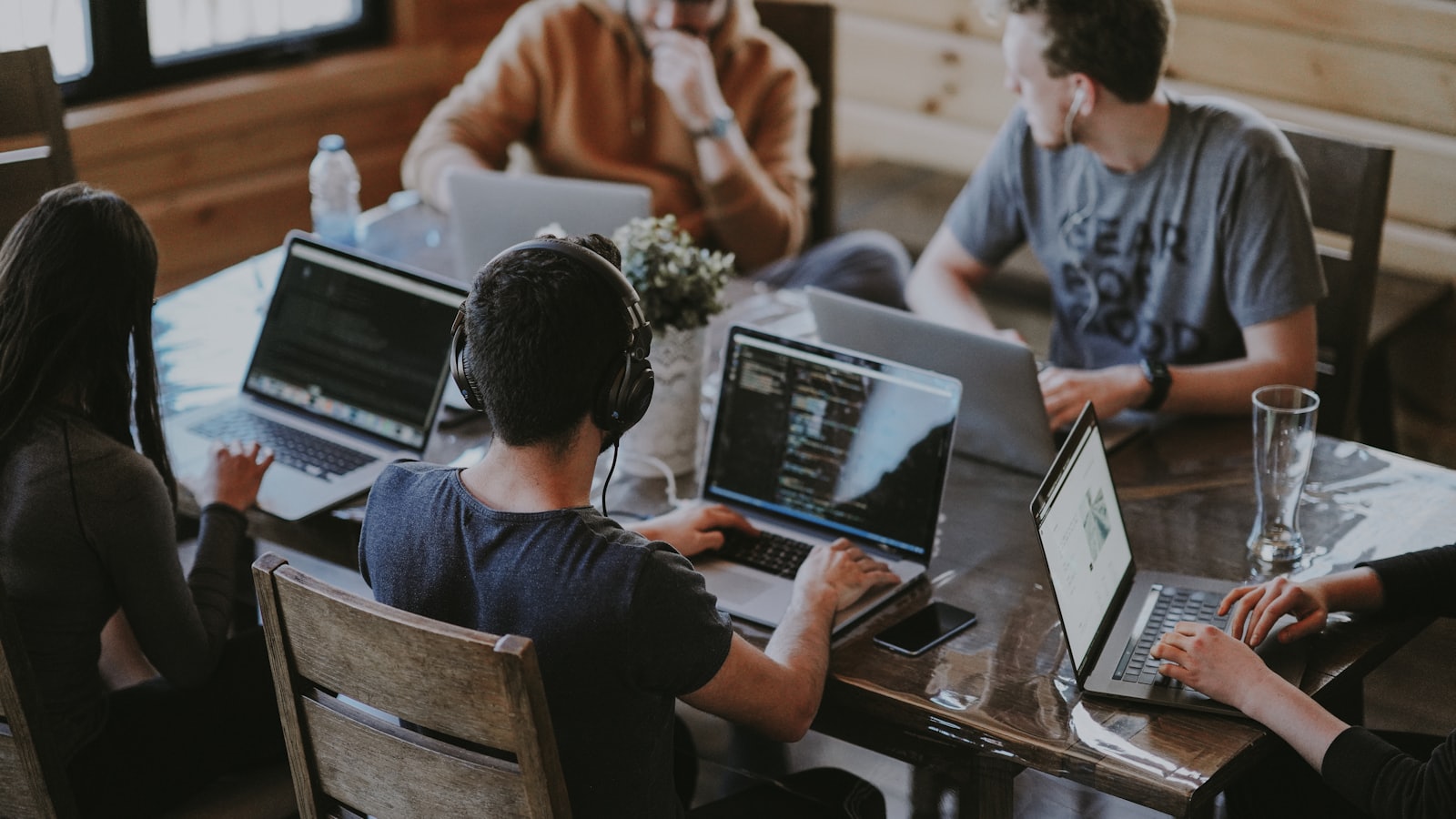 Een team developers werkt samen rond een tafel vol laptops.